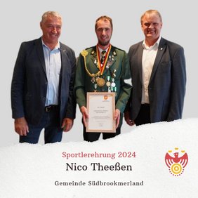 Drei Personen lächeln in die Kamera. Eine Person hält eine Urkunde und trägt eine Medaille um den Hals