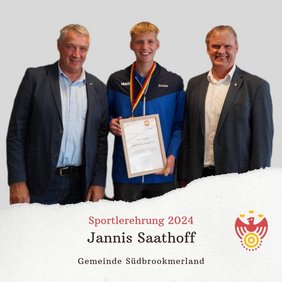 Drei Personen lächeln in die Kamera. Eine Person hält eine Urkunde und trägt eine Medaille um den Hals