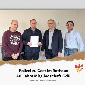 Vier Personen lächeln in die Kamera. Eine Person hält ein Dokument
